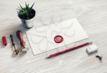 Blank retro stationery. Vintage envelope with wax seal, stamp, pencil, eraser, plant and spoon on light wood table background.