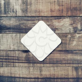 Blank square beer coaster on vintage wooden background. Flat lay.