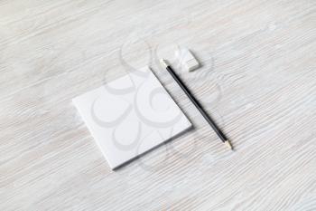 Blank white square brochure, pencil and eraser on light wooden background. Responsive design mockup.