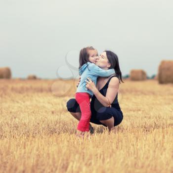 Photo of mother and her daughter child girl hugging in the field on straw bales background. Happy loving family. Selective focus. Toned image.
