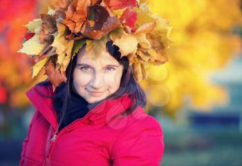 Pretty young woman with a wreath of autumn maple leaves on the head. Woman and autumn. Selective focus. Toned image.