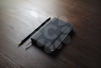 Black notebook and pencil on wooden background. Responsive design mockup.