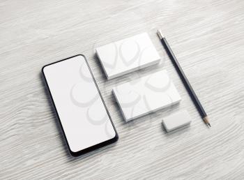 Branding mock up. Smartphone, blank business cards, pencil and eraser on light wood table background. Responsive design template.