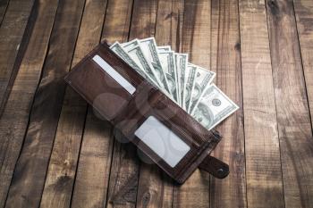Money in a leather wallet on wooden background. One hundred dollar bills.