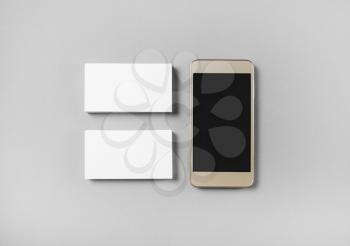Two stacks of blank business cards and cellphone with blank screen on gray paper background. Top view.