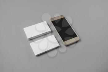 Smartphone and blank business cards on gray paper background. Template for branding identity.