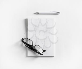 Photo of blank notebook, glasses and pen on white paper background. Flat lay.