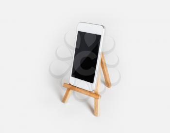 Smartphone with blank screen on wooden stand at white paper background. Mockup for placing your design