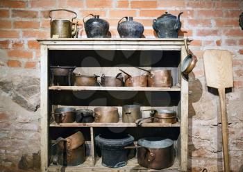 Vintage copper and cast-iron cookware: pans, pots, casseroles on wooden shelfs on old brick wall background. Ancient kitchen utensil.