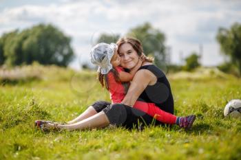 Mother and daughter are hugging. Mom and child girl sitting on grass outdoors. Happy loving family. Selective focus.
