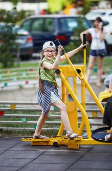 Child girl is engaged with a sports training apparatus outdoors. Sportive child on exercise machine. Healthy lifestyle concept. Selective focus.