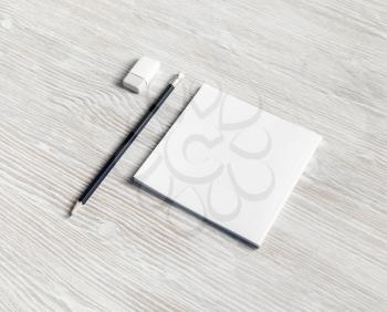 Photo of white square booklet, pencil and eraser on light wood table background.
