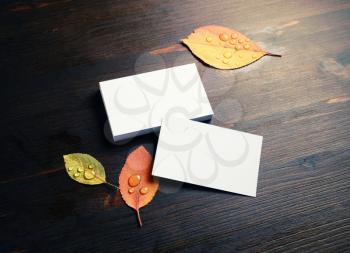 Blank white business cards and autumn leaves on wooden background.
