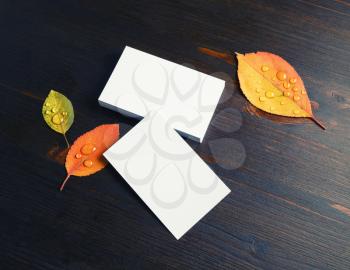 Blank business cards and autumn leaves on wood table background. Mockup for branding identity.