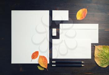 Photo of blank stationery set and autumn leaves on wooden background. Corporate stationery template. Flat lay.