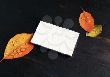 Blank business card and autumn leaves on wood table background.