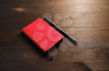 Red notepad and pencil on wood table background. Template for branding identity.