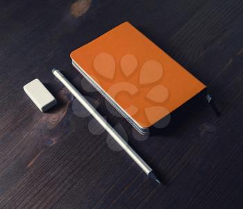 Orange notepad, pencil and eraser on wooden table.
