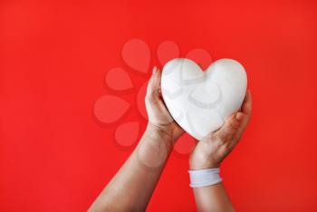 White heart in female hands on red background.