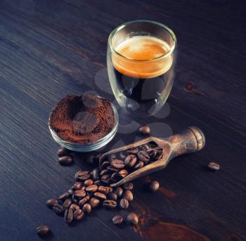 Espresso on vintage wooden kitchen table background. Coffee cup, roasted coffee beans and ground powder.