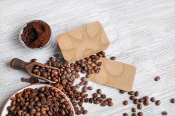 Coffee beans, blank kraft business cards and coffee ground on light wooden background.