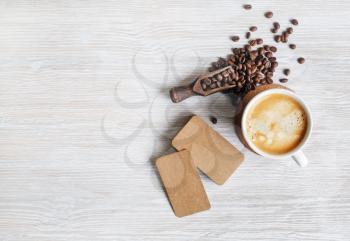 Coffee cup, roasted coffee beans and blank kraft paper business cards on light wood table background. Top view with copy space for your text. Flat lay.