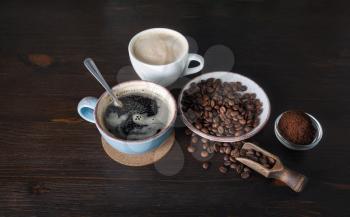 Coffee cups, roasted coffee beans and ground powder on wood kitchen table background.