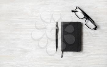 Black notepad, glasses and pencil on light wood table background. Copy space for your text. Flat lay.