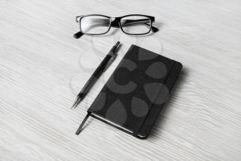 Photo of closed blank black notepad, glasses and mechanical pencil on light wood table background. Template for placing your design.