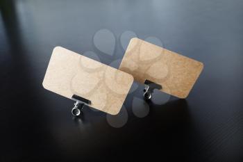 Photo of blank kraft business cards and metal binder clips on black wood table background.