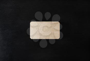 Photo of blank kraft business card on black wooden background. Mock-up for branding identity. Flat lay.