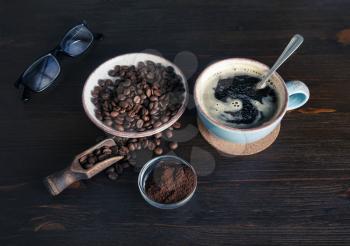 Photo of fresh tasty coffee on wooden background. Coffee cup, coffee beans, ground powder and glasses.