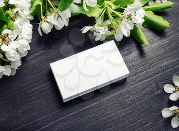 Photo of blank business cards with spring flowers on wooden background. Mockup for branding ID.