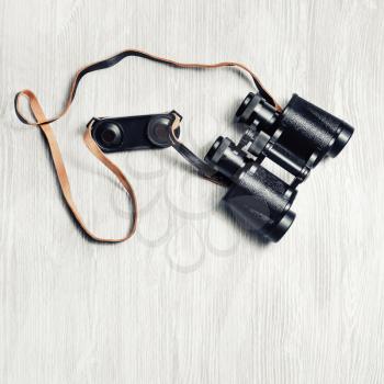 Black retro binocular against light wooden background. Top view. Flat lay.