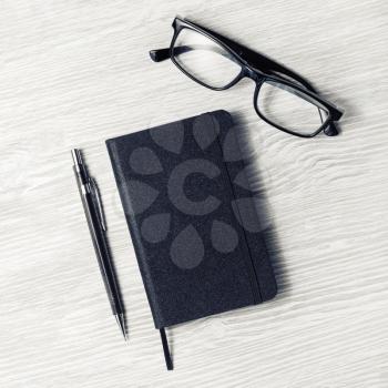 Black notebook, glasses and mechanical pencil on light wooden background. Top view. Flat lay.