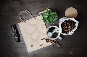 Kraft stationery and coffee. Vintage paper bag, coffee cup, coffee beans, glasses, pen and plant on wood table background. Flat lay.