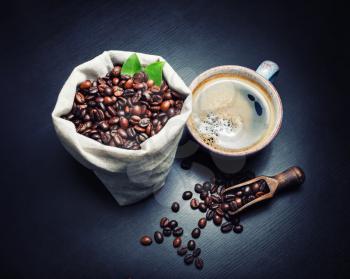 Delicious fresh coffee. Coffee cup and roasted coffee beans on black wooden kitchen table background.