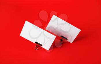 Photo of blank business cards and metal binder clips on red paper background.