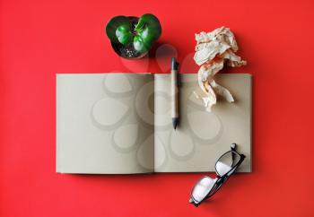 Blank booklet and stationery on red paper background. Book, glasses, pen, crumpled paper and plant. Responsive design mockup. Flat lay.