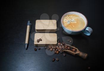 Blank kraft business cards, coffee cup, pen and coffee beans on black wood table background.