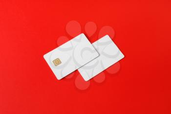 Two blank credit cards on red paper background. Photo of white bank cards. Mockup for branding identity.