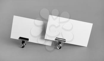 Two blank business cards and metal binder clips on gray background. Mockup for branding identity.