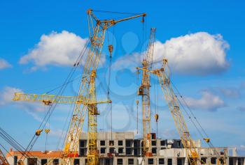 Yellow cranes are building a multi-storey house against the blue sky background.