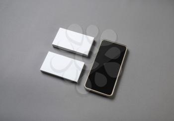 Smartphone and blank business cards on gray paper background. Blank branding mockup.
