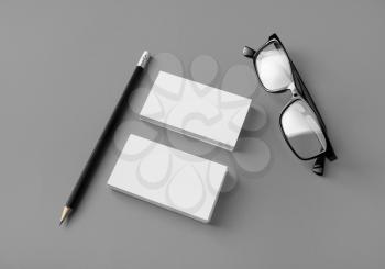 Blank business cards, pencil and glasses on gray paper background. Mockup for ID.