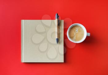 Photo of blank closed booklet, pen and coffee cup on red paper background. Responsive design mockup. Stationery set. Template for placing your design. Flat lay.