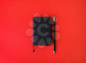Photo of blank black notebook and pencil on red paper background. Responsive design template. Top view. Flat lay.