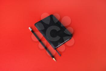 Black notebook and pencil on red paper background. Space for your text.