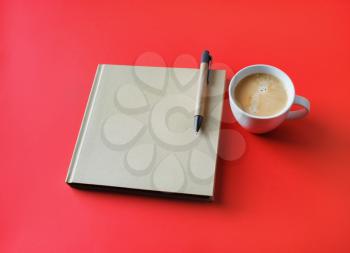 Photo of closed blank square book, coffee cup and pen on red paper background. Template for placing your design.