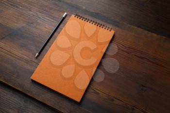 Blank orange notebook and pencil on wood table background. Responsive design mockup.